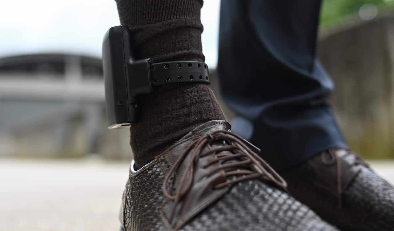 Electronic ankle bracelet on top of a black sock and brown shoe