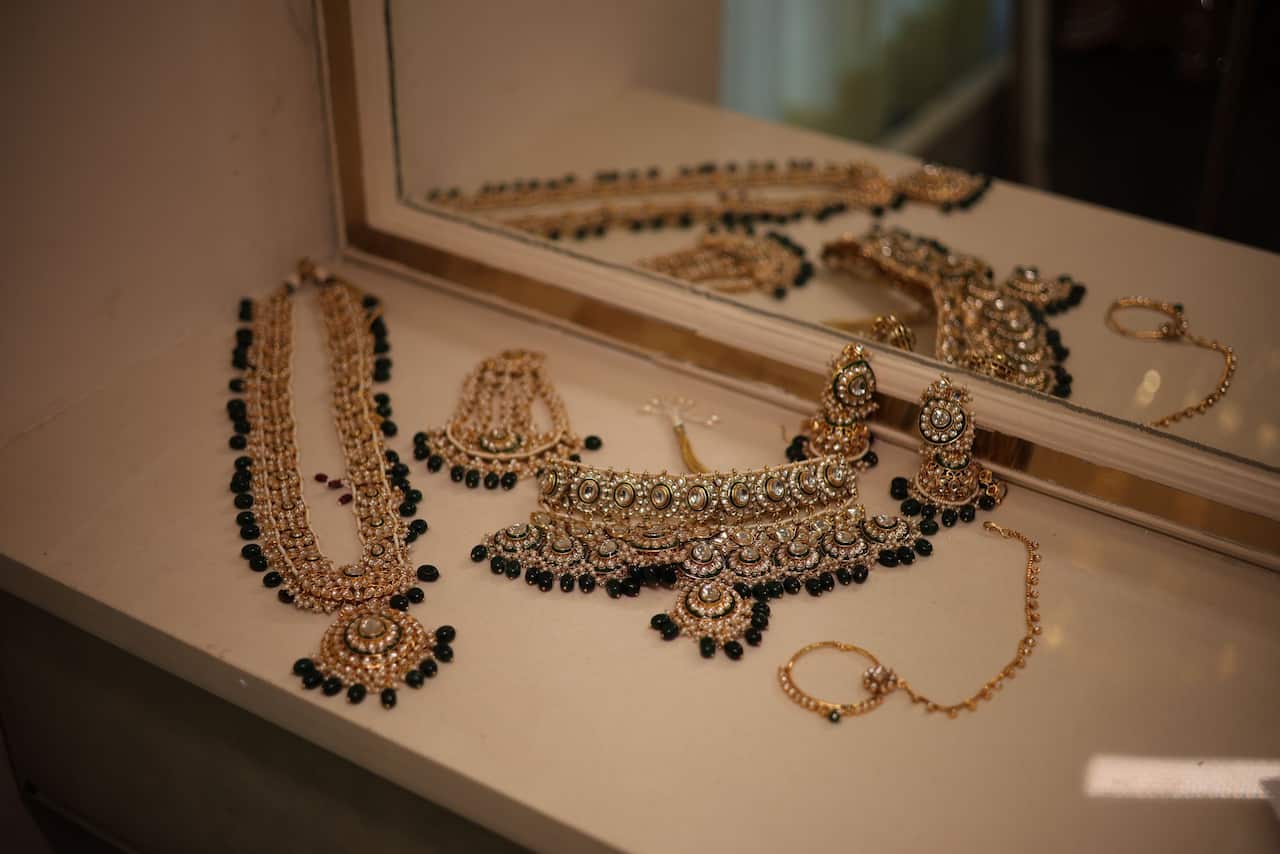 Gold jewellery lying on a table next to a mirror.