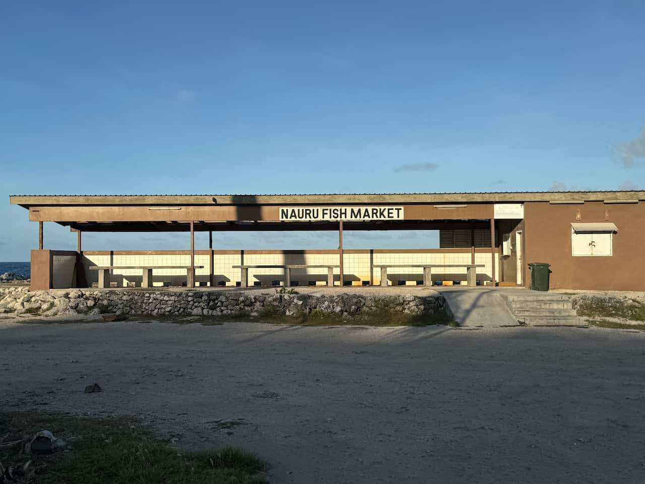 A wooden structure at a distance, labelled 'Nauru fish market,' with cemented land in the foreground.
