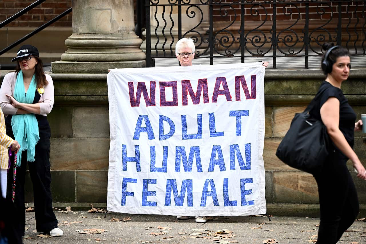 A person stands outside court with a sign that reads 'Woman Adult Human Female'.