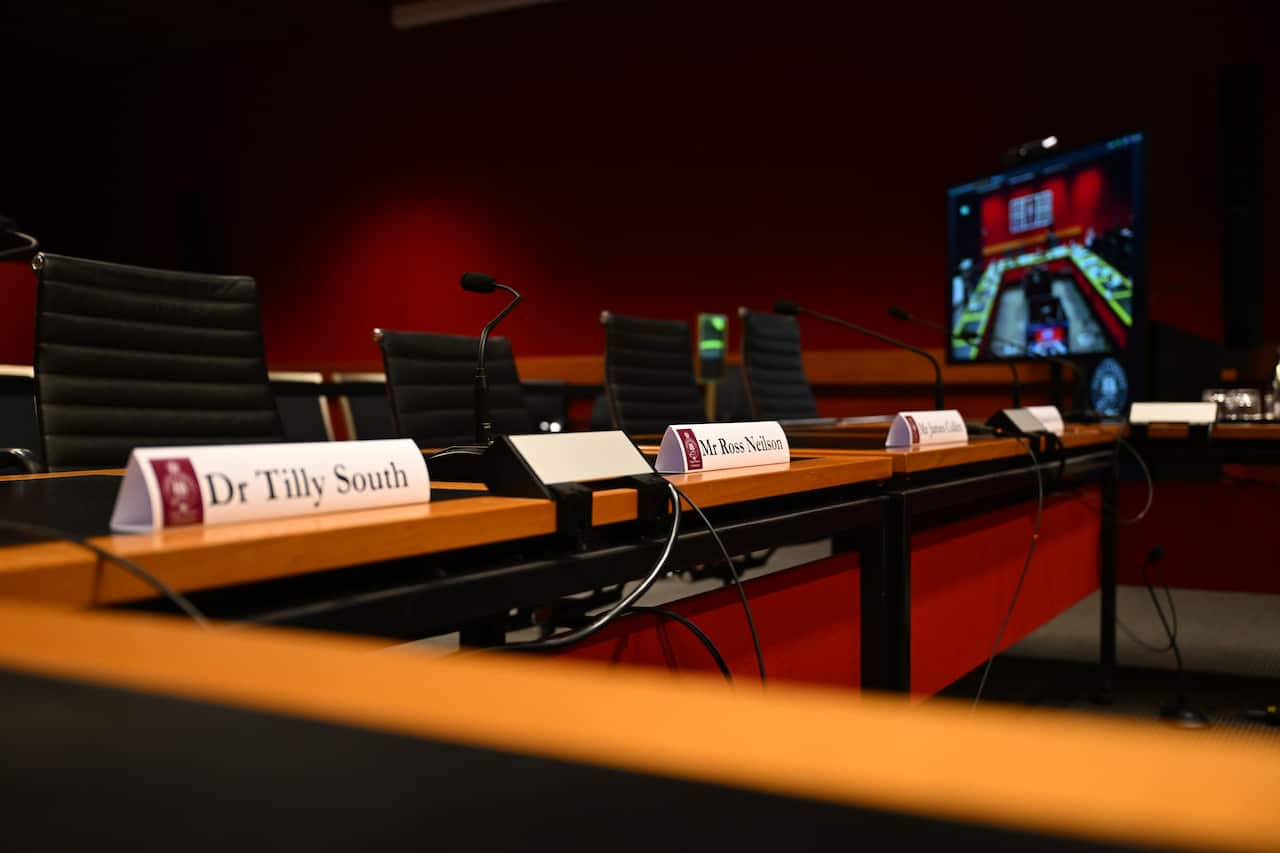 A row of empty seats behind a table, with cards listing people's names in front of them.