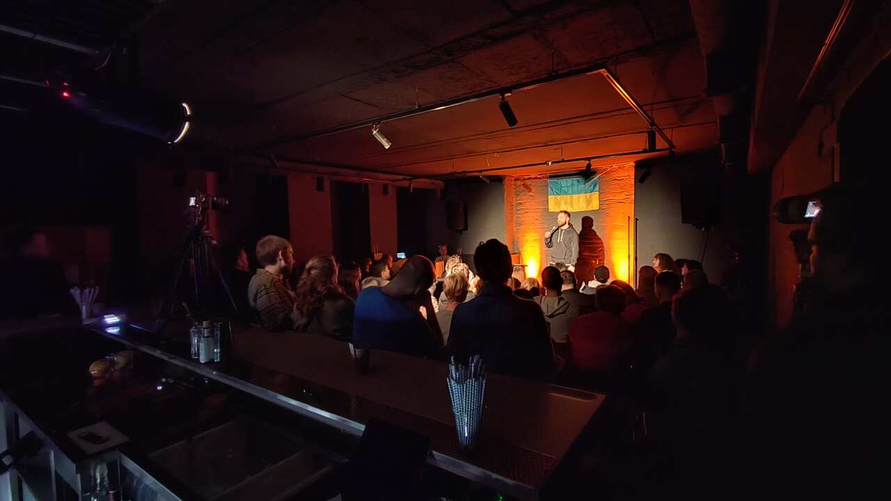 A man stands on a stage in front of a small audience 