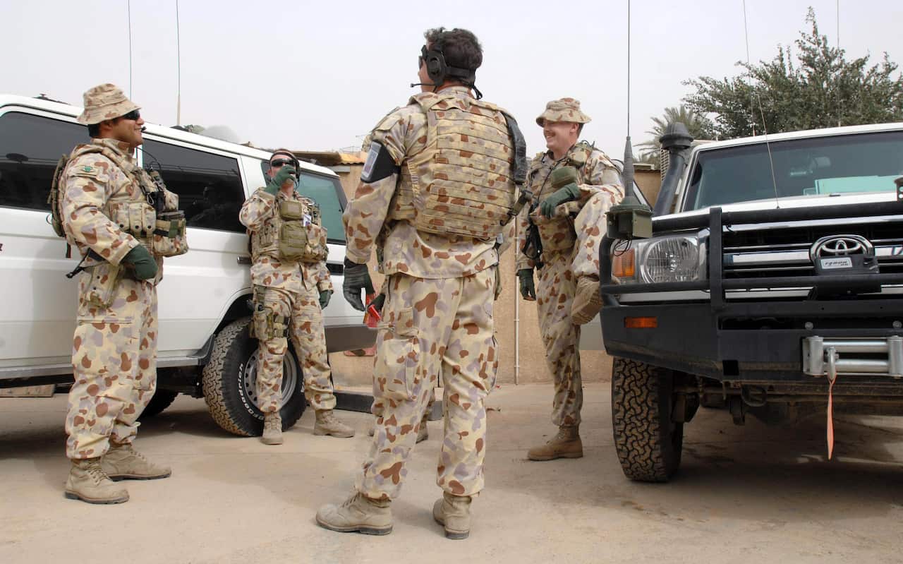 A photo of four Australian soldiers standing between two vehicles, chatting and laughing.