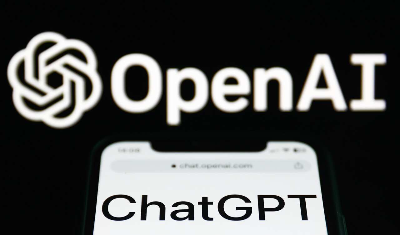 ChatGPT website displayed on a phone screen and OpenAI logo displayed on a screen in the background 