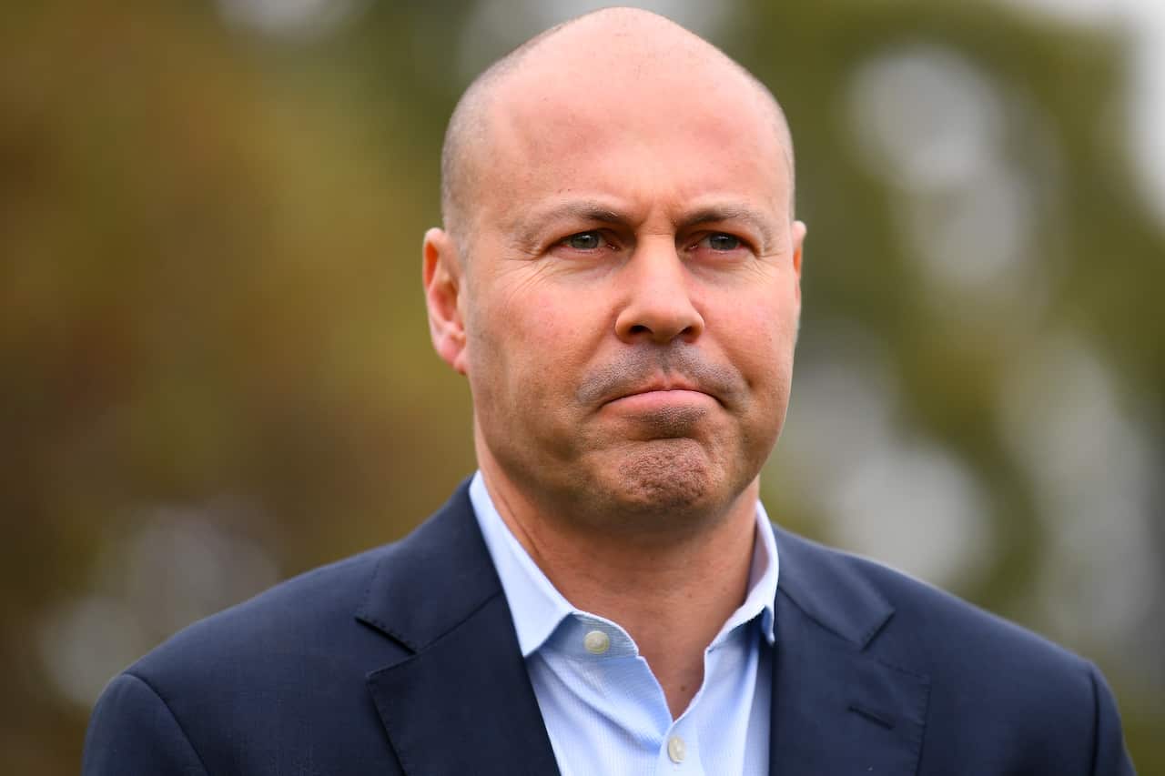 Man in suit stands in front of trees.