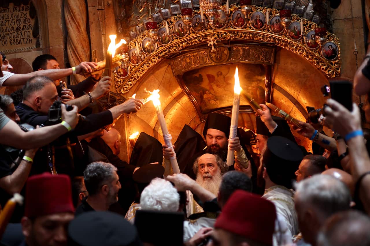 Two religious men holding large lit candles moving towards a group of people in a building