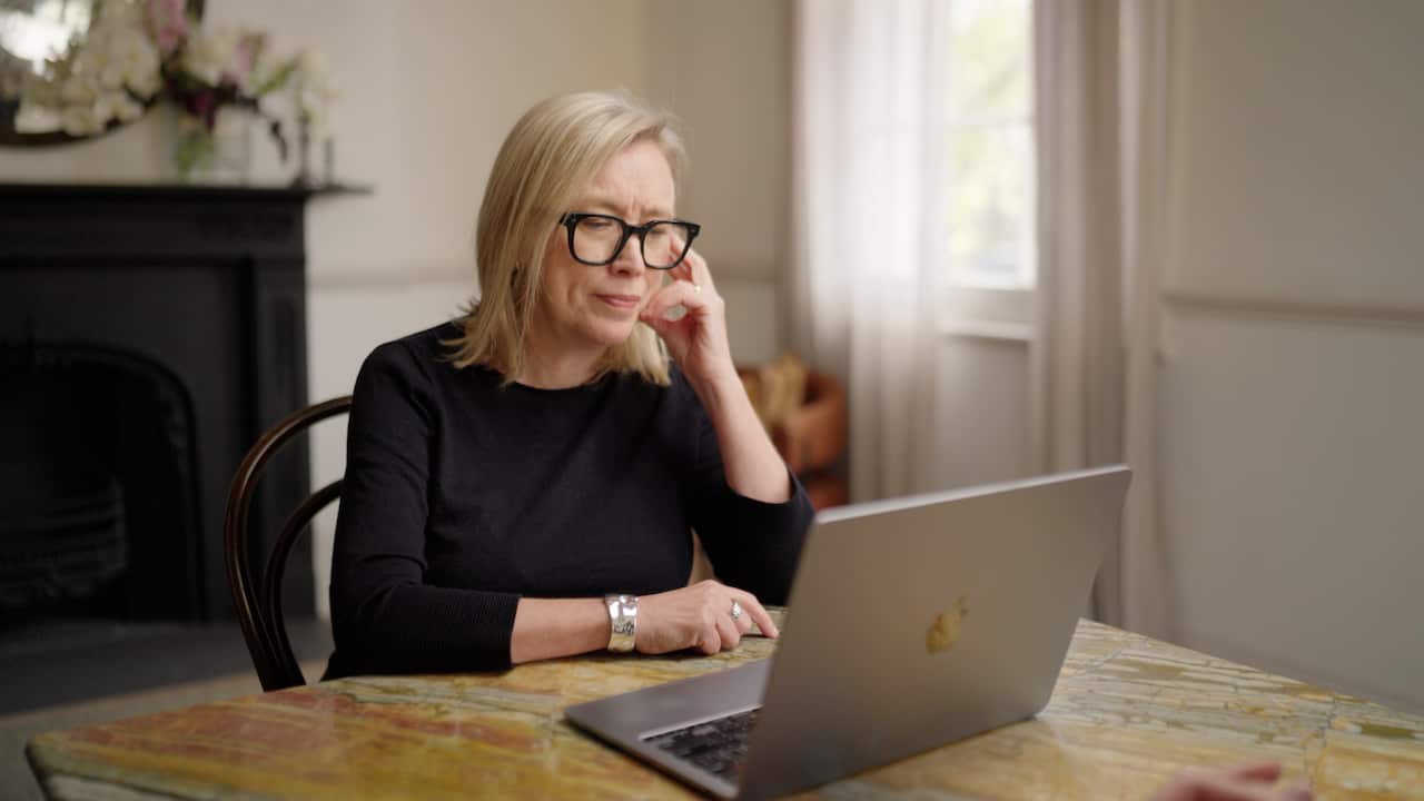 A woman in glasses looks at a laptop.