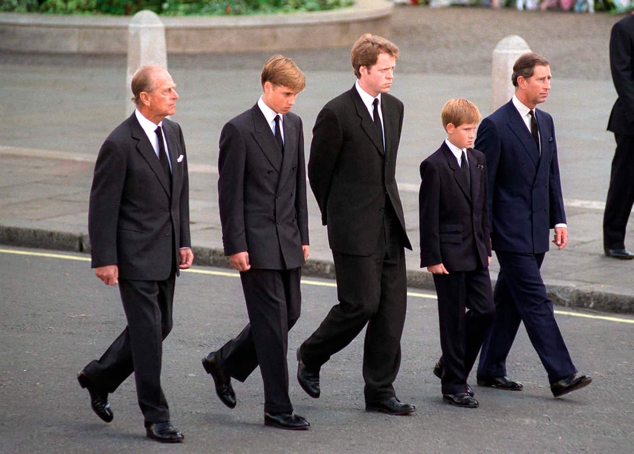 Five people, three men and two boys, walking behind a funeral procession. 