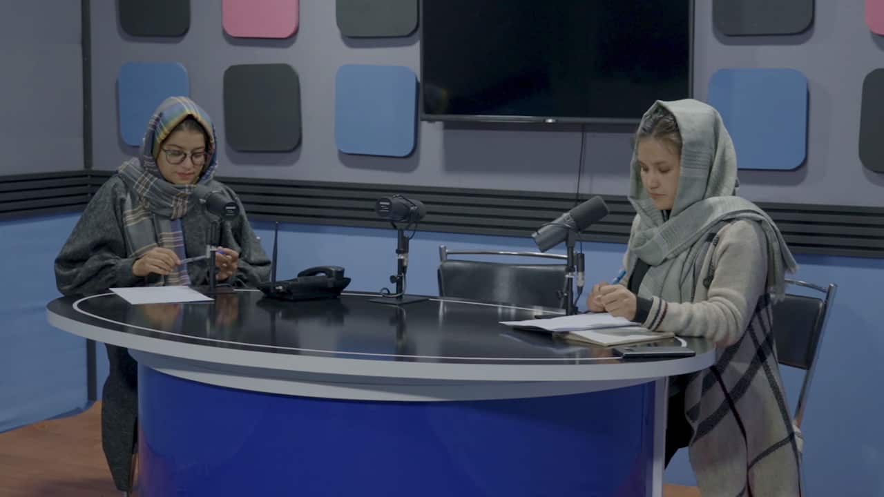 Two young women wearing headscarves sit in front of microphones in a radio studio