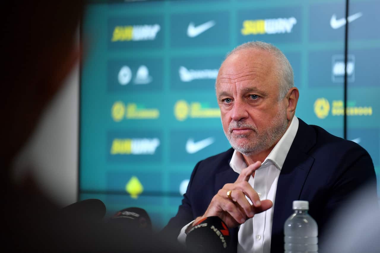 A man in a black suit speaks to the media during a press conference.