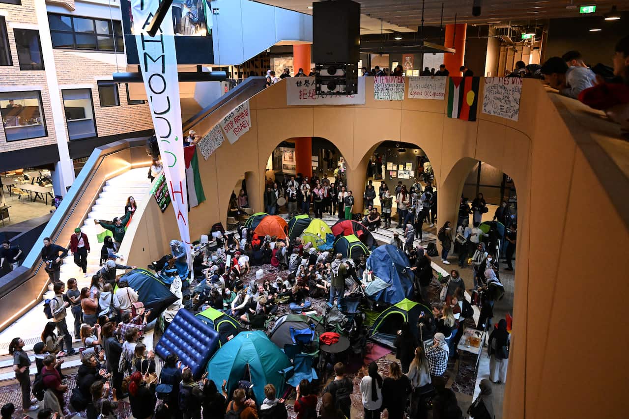 Students gather with tents and banners during a protest inside a university building.