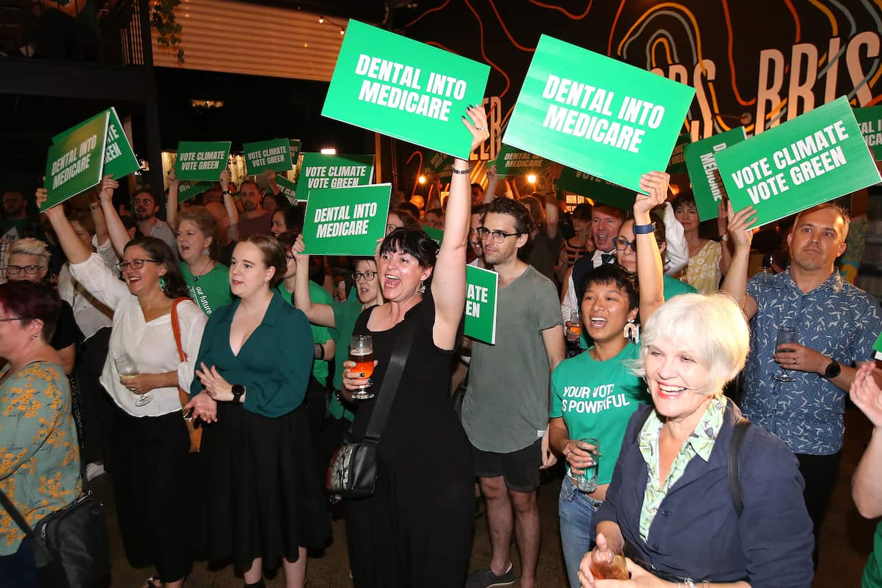 People are seen cheering while holding signs that read "Dental into Medicare" and "Vote climate vote Green".