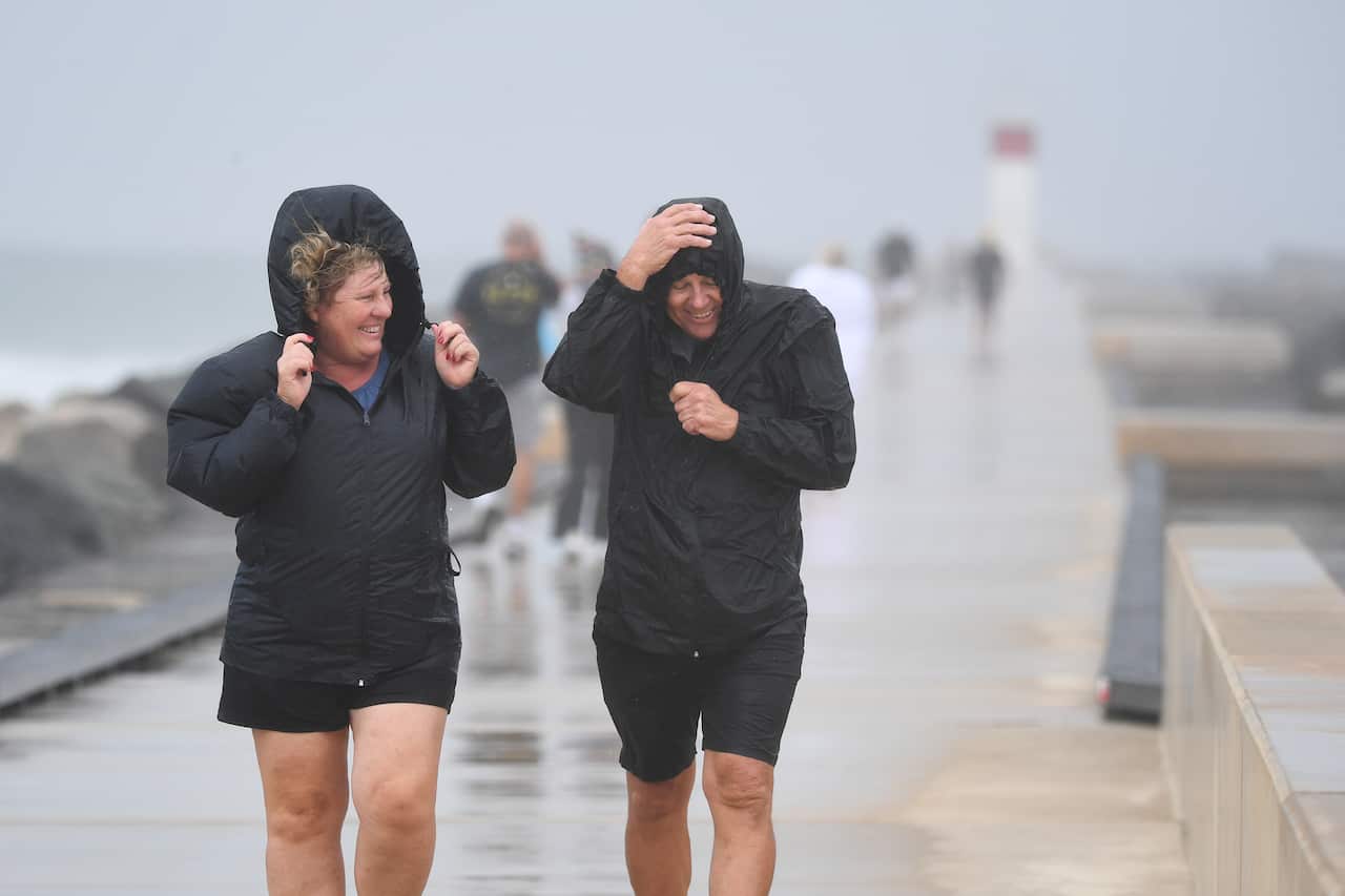 Two people walk on a boardwalk as rain falls.