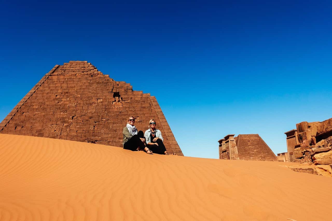 Two women sit in front of the Pyramids of Meroe in Sudan.