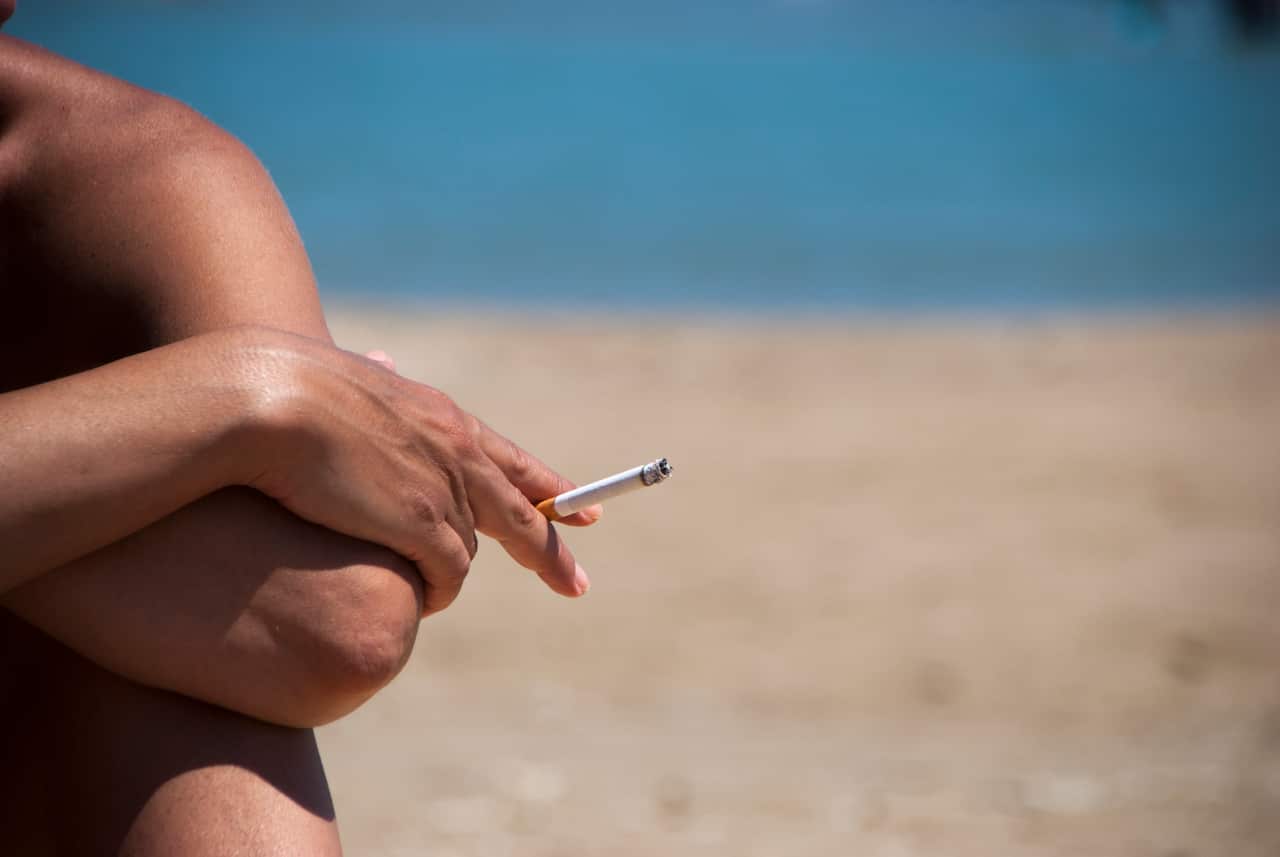 A person smoking a cigarette at a beach.