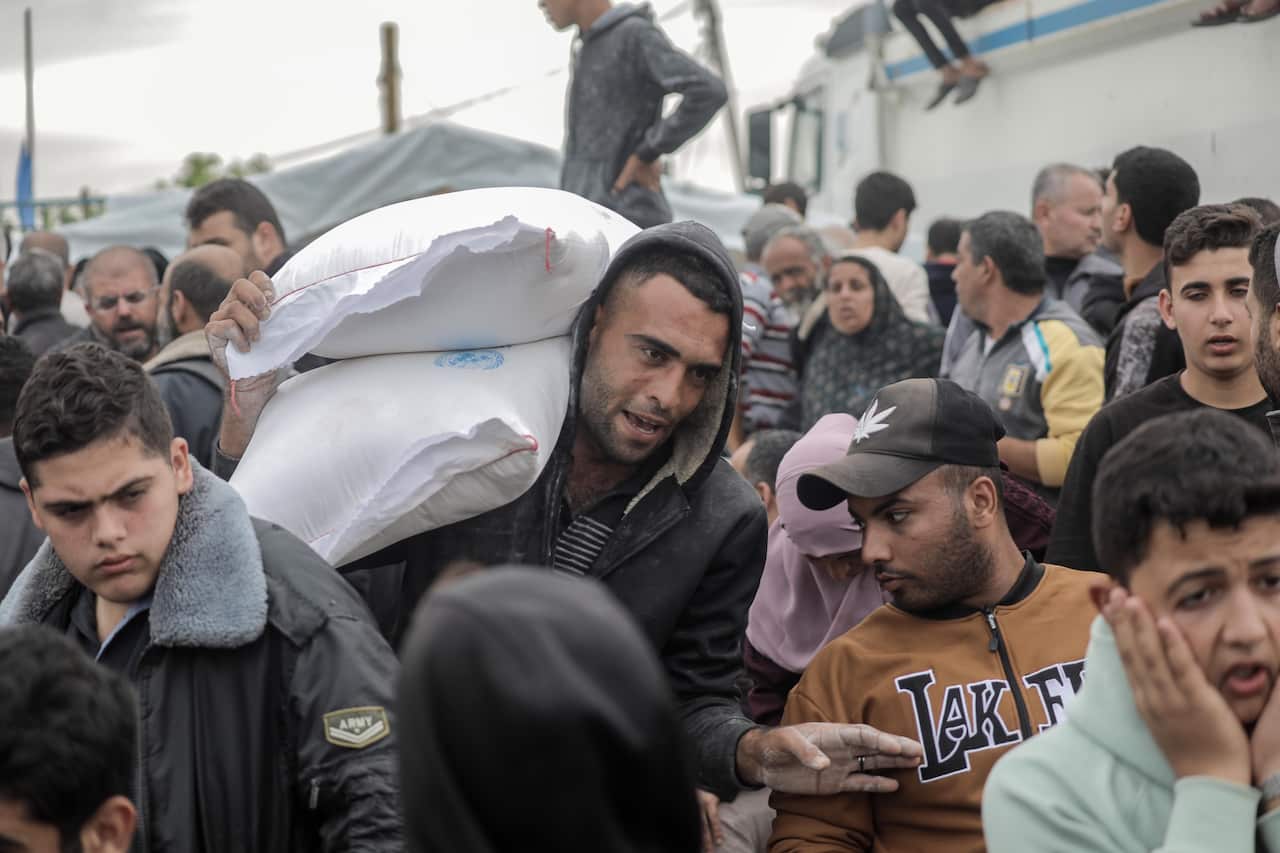 A large group of people, one with two white bags of supplies.