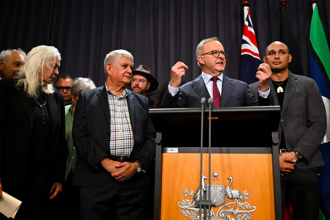 Man speaking at lectern surrounded by supporters.