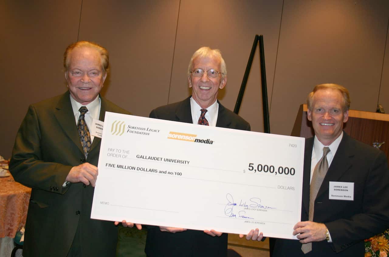 Three men, wearing suits and ties, holding a large check for US$5 million.