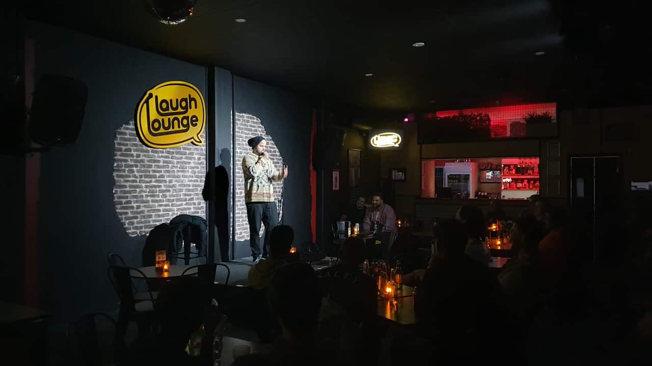 A man spotlighted on stage in front of a darkened audience.