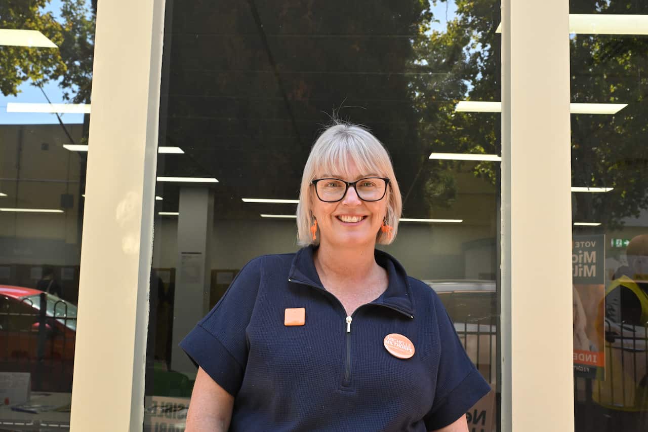 A woman wearing a black polo shirt standing in front of large windows