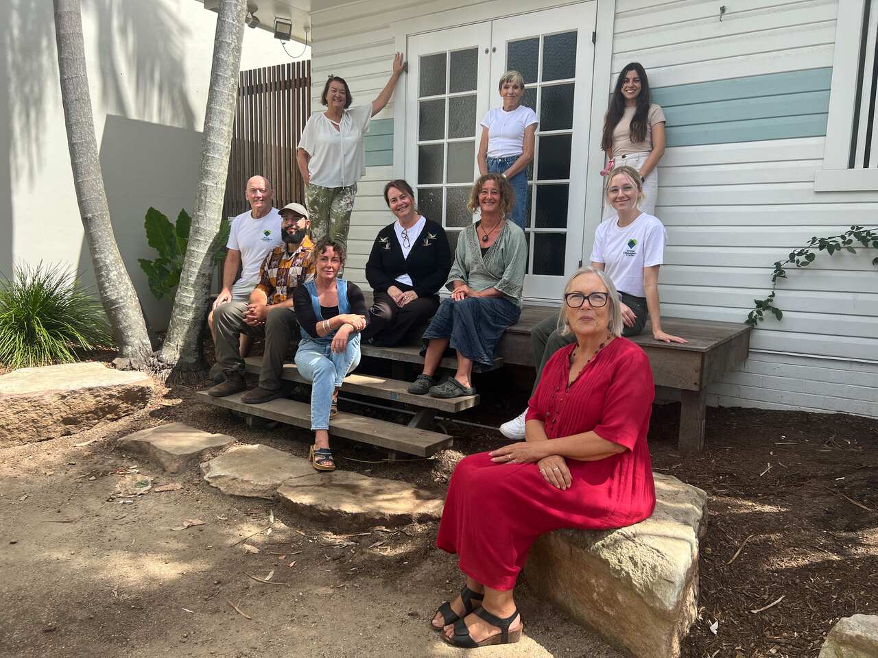 A photo showing the staff at the Fletcher Street Cottage sitting on rocks and stairs in front of the building.
