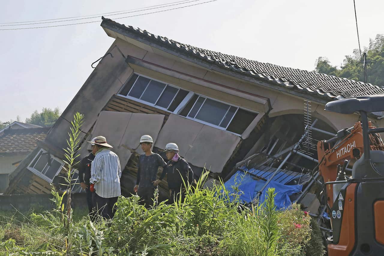 Officials inspect a collapsed house leaning very heavily on its side.