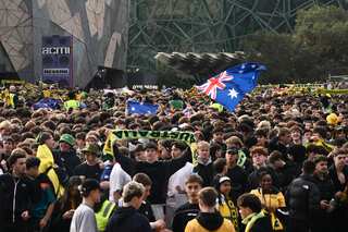 A crowd of people waving Australian flags, with green and gold scarves being waved.