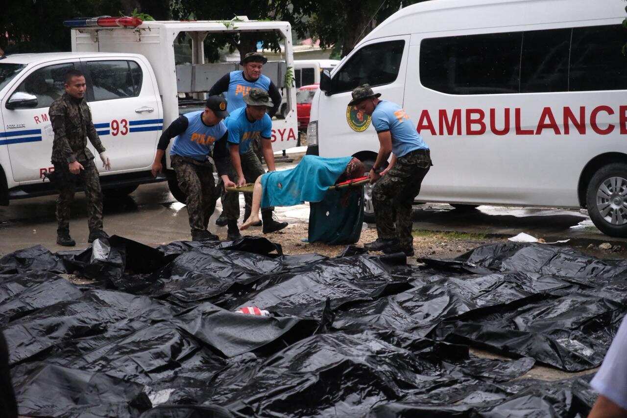 Policemen carry a victim past cadaver bags in the aftermath of an earthquake.