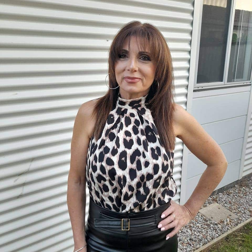 A woman with brown hair standing outside with her hand on her hip