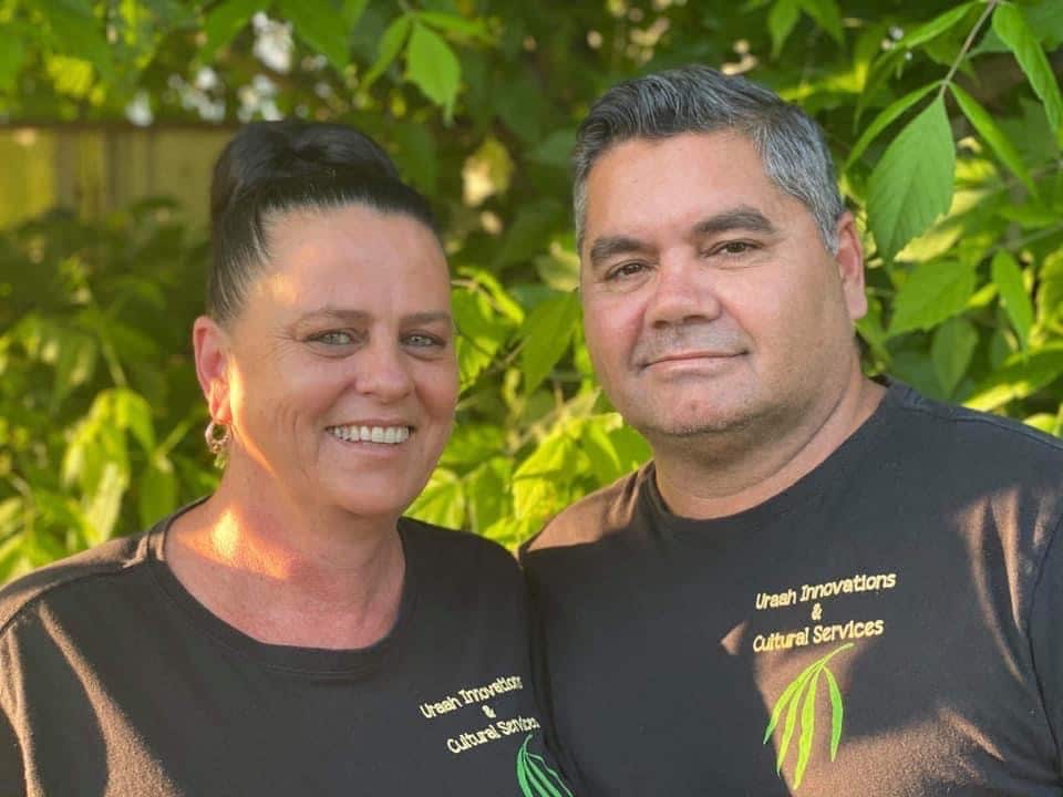 Headshots of Michelle and Ted smiling in a leafy area and wearing black t-shirts with the logo "Uraah Innovations & cultural services" and a gum leaf