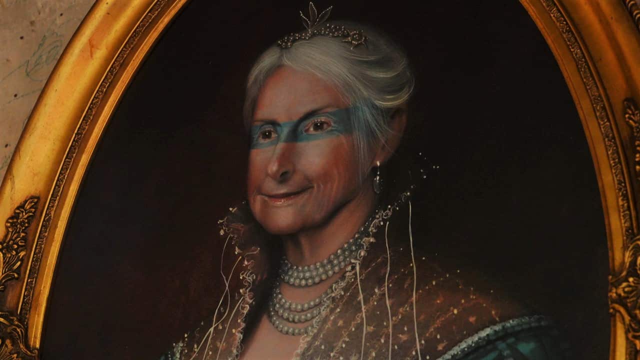 A close up on a painted portrait of Diana Shaw, stylised in a medieval style with ornate period outfit, pearls, a blue shadow over the eyes, and a detailed golden frame.
