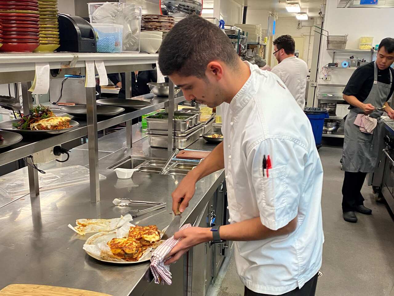 A man in chef's clothing in a kitchen plating food.