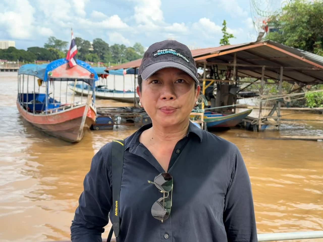 A woman wearing a grey long sleeved polo shirt and a grey cap standing in front of a muddy river