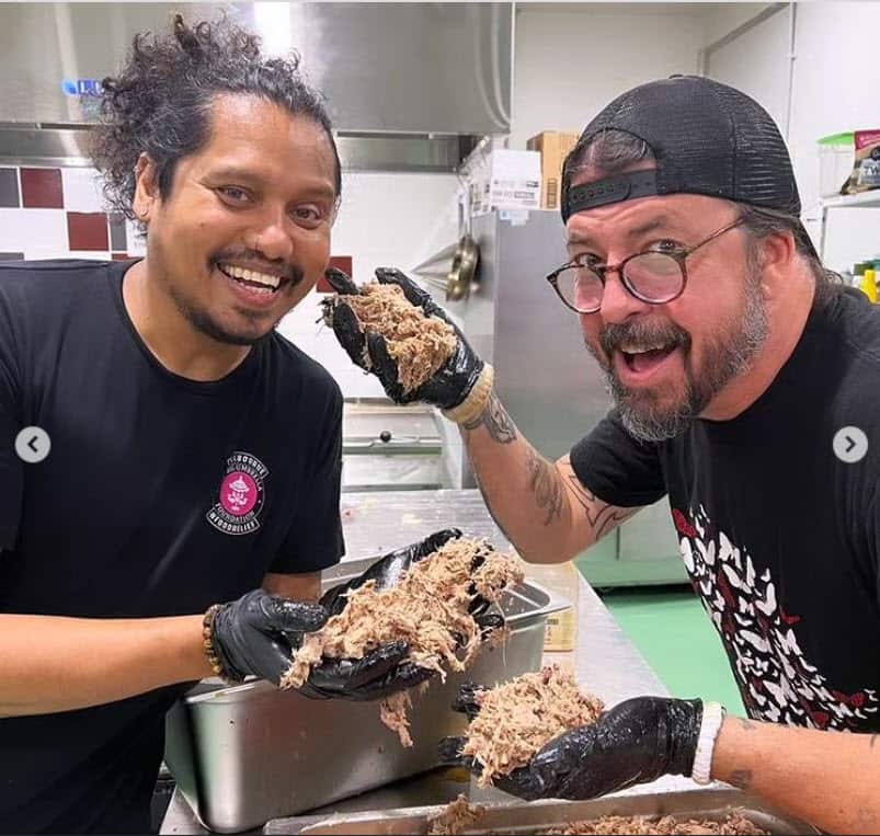 Dave Grohl and another volunteer wearing black gloves, preparing shredded meat in a kitchen.