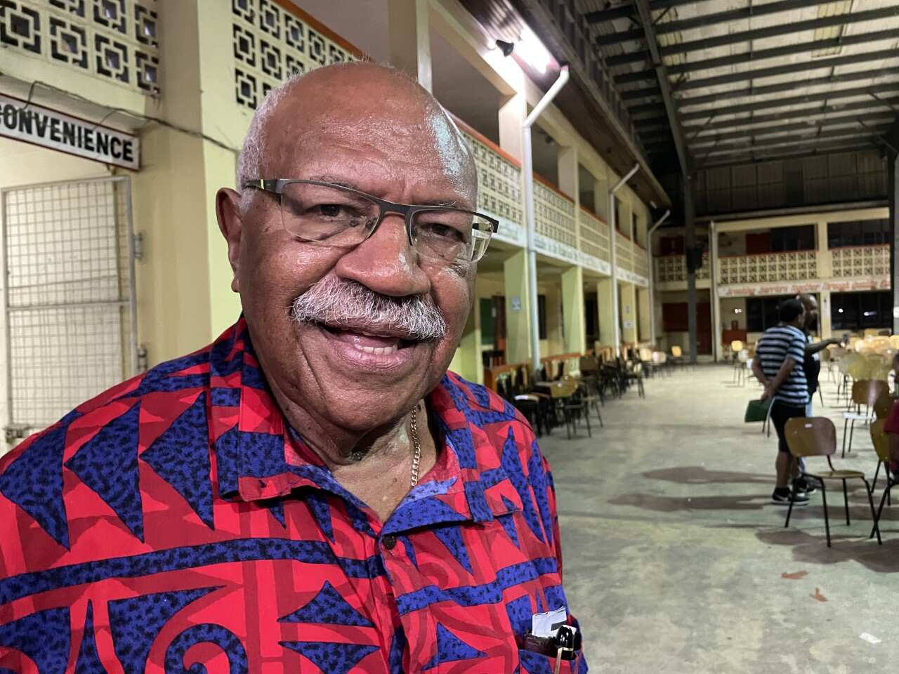 A man standing inside wearing a red and blue patterned shirt