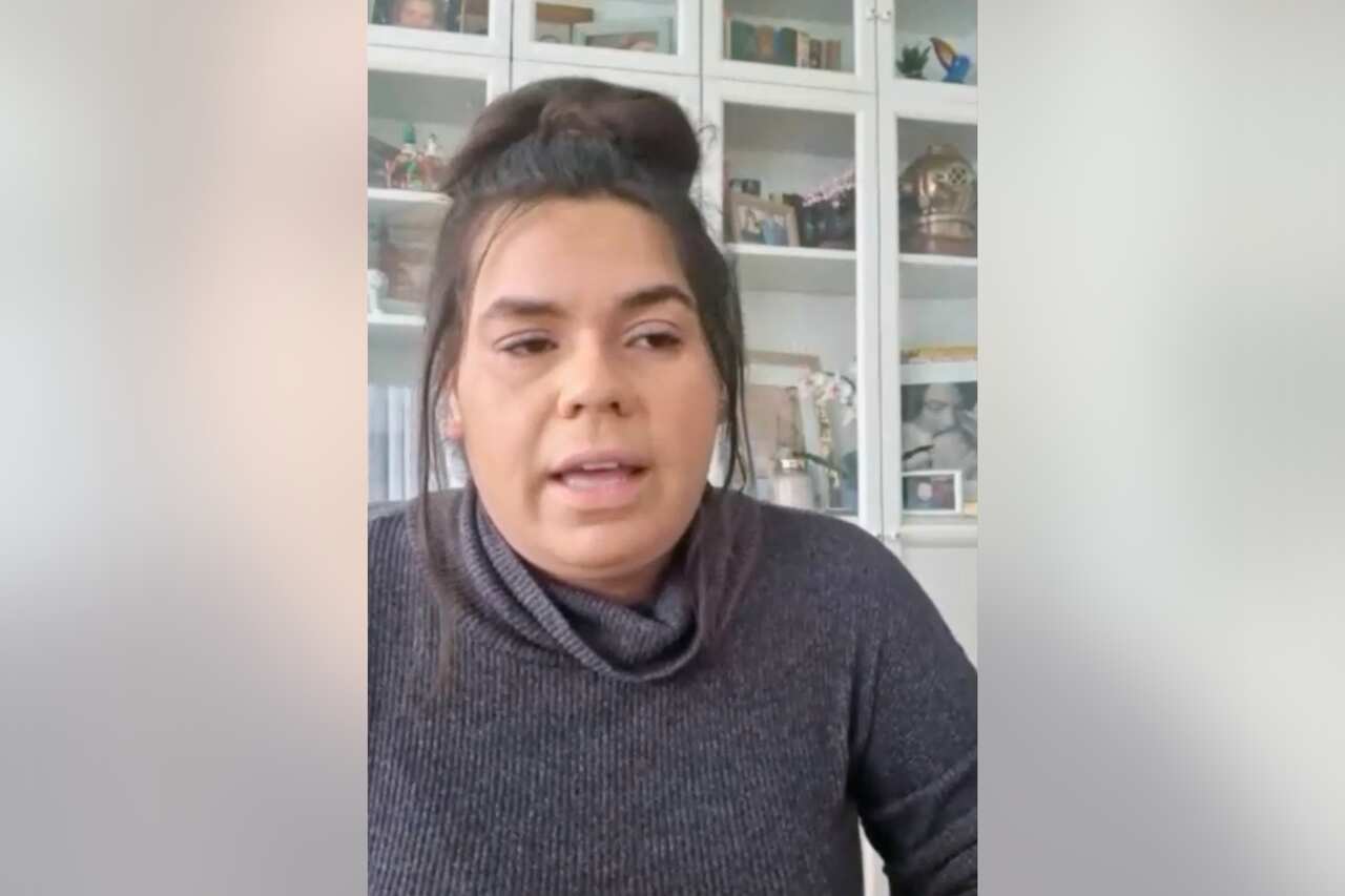 A woman speaking in front of a glass cabinet.