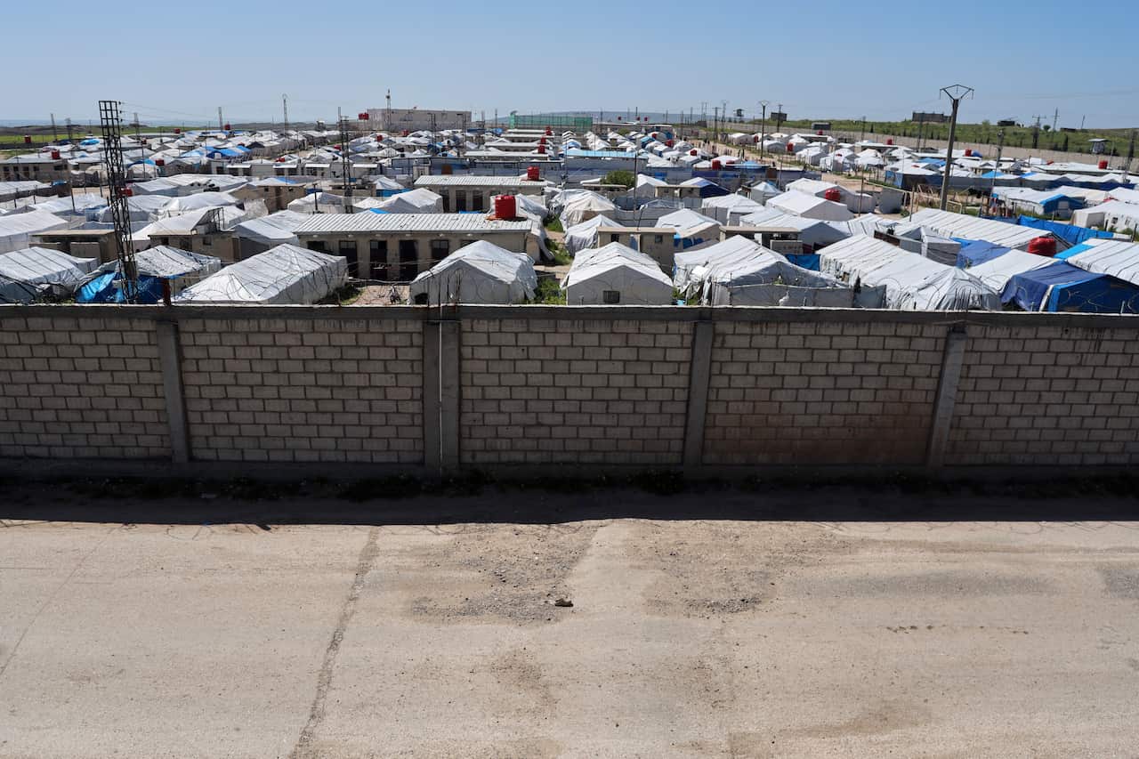 A brick wall surrounds a tent camp housing refugees.