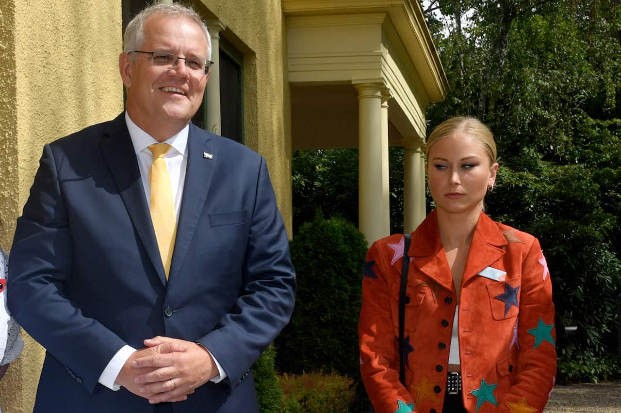 A man in a suit smiles standing next to a young woman in an orange jacket with a starry design.