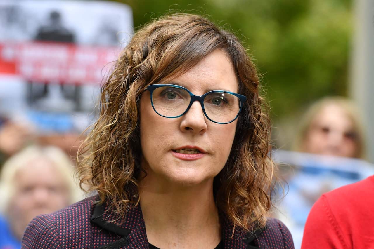 A woman with curly hair and wearing glasses speaks