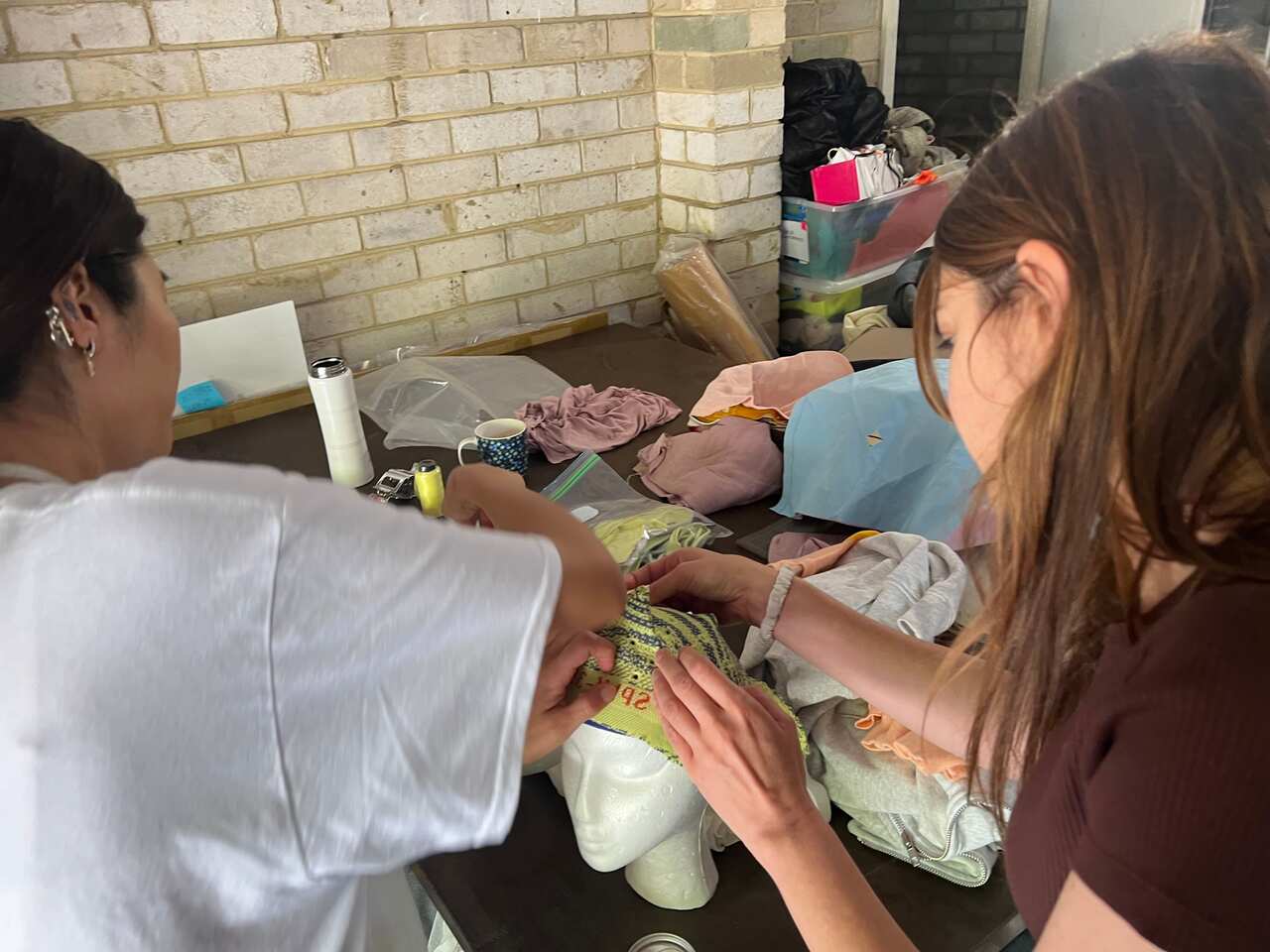 Girls sew a cap on a mannequin head. 