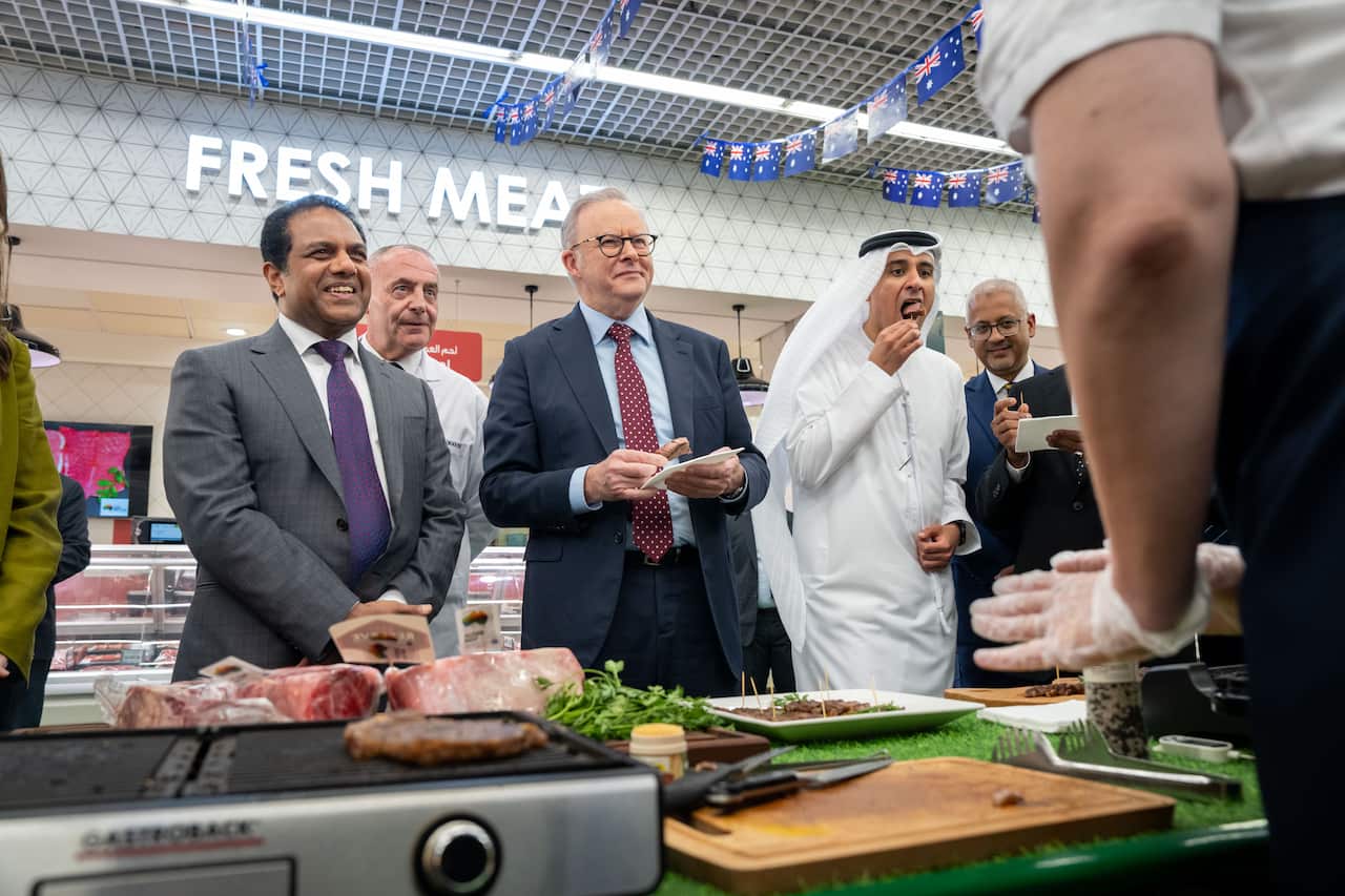 Three men stand in front of a meat stand inside a supermarket.