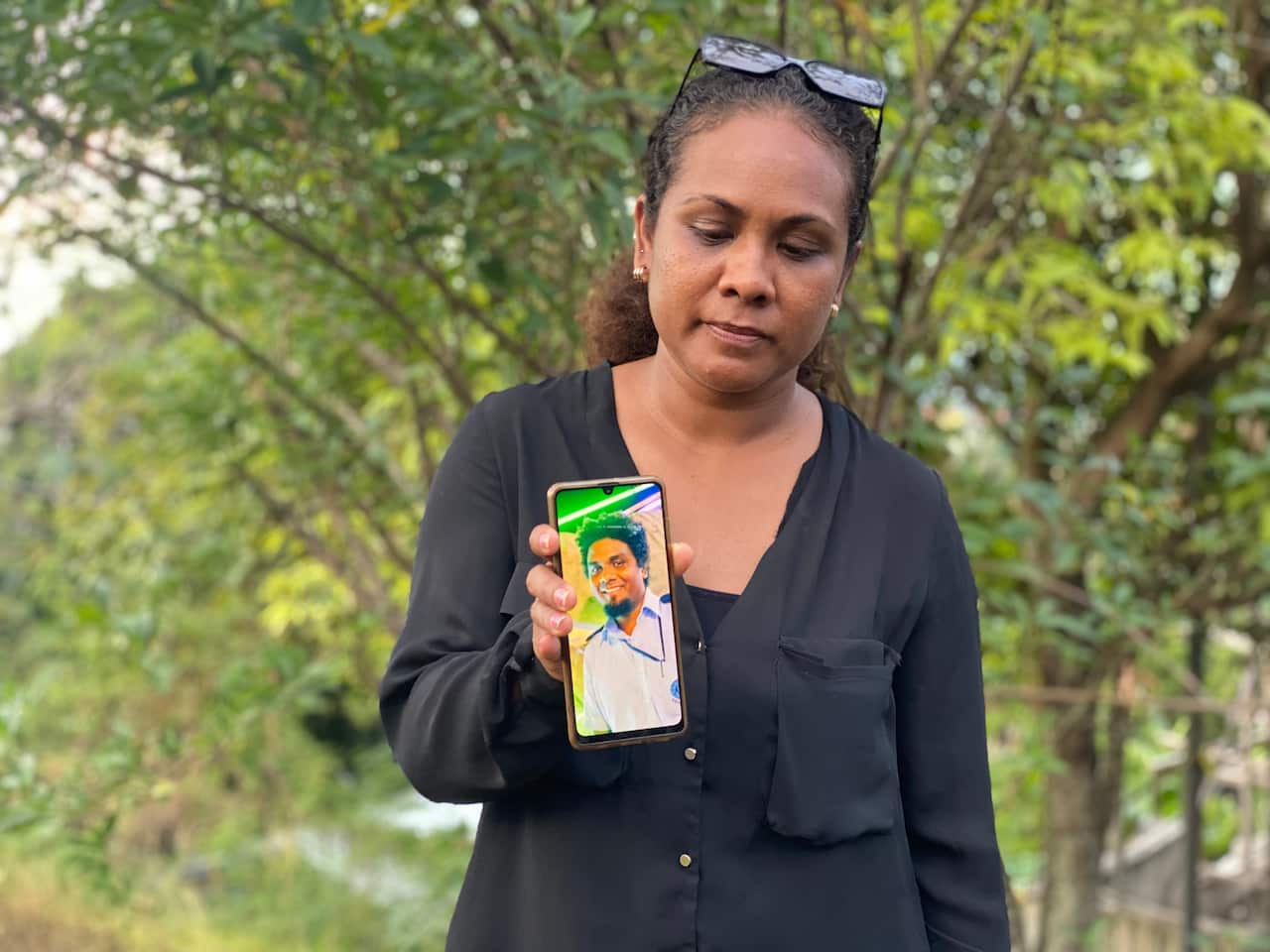 Woman standing outside and holding a mobile phone displaying a photograph 