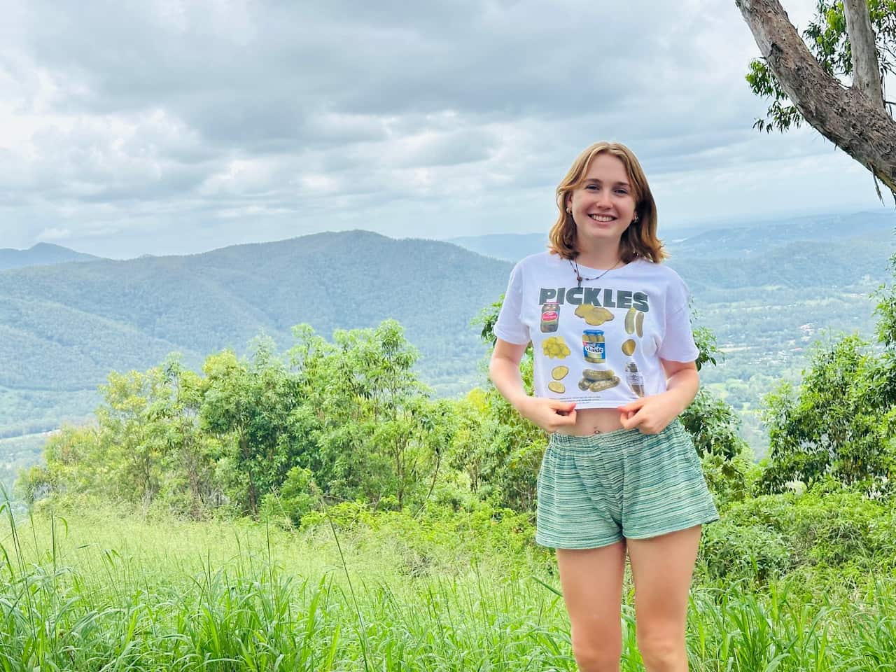 
A girl stands in a green field overlooking mountains.
