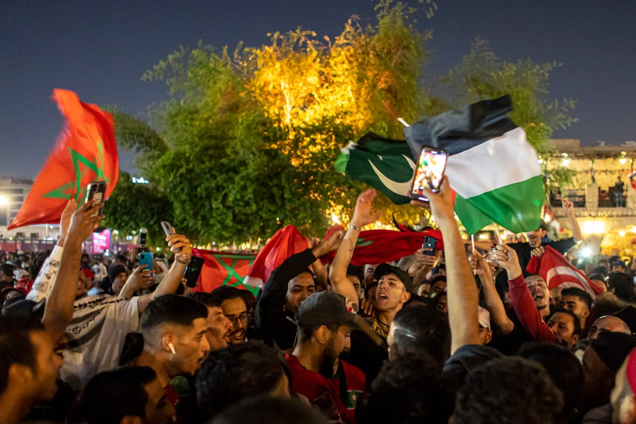 A crown of people celebrating. Some are waving the flags of Morocco and Palestine.
