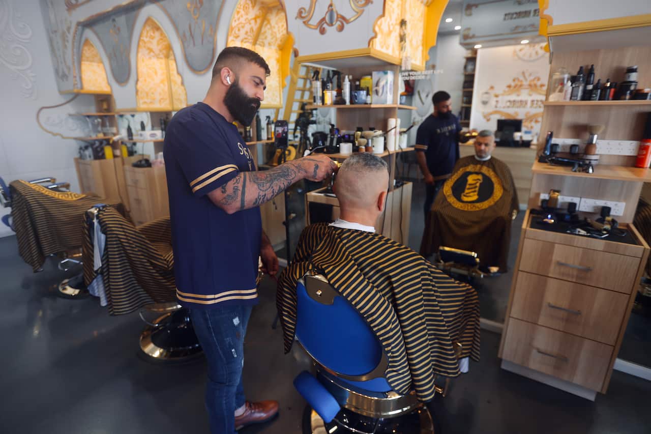 Barber giving a haircut to a customer, who is sitting in a chair.
