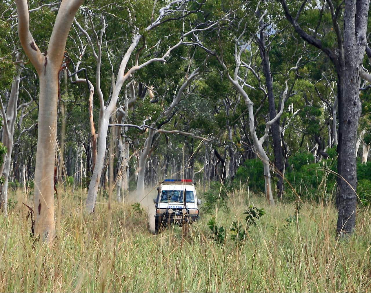 A police SUV drives through a grassy woodland area.