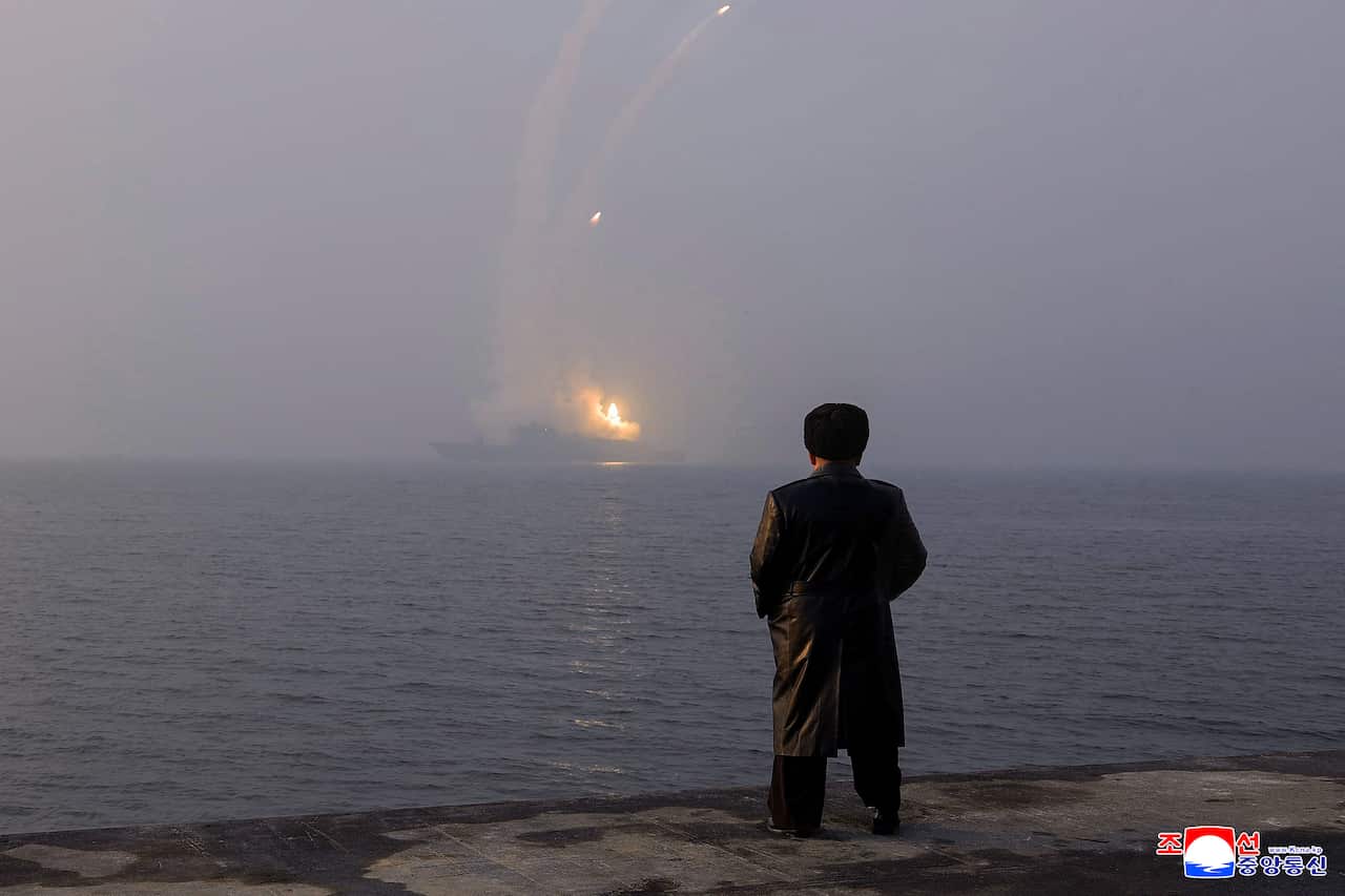 A silhouette of a man watching a war ship fire missiles at a distance.