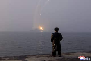 A silhouette of a man watching a war ship fire missiles at a distance.