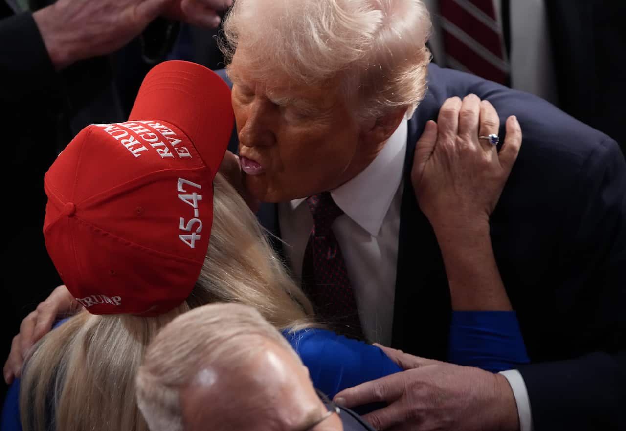 Trump cheek-kissing Marjorie Taylor Greene, who is wearing a red Trump hat..