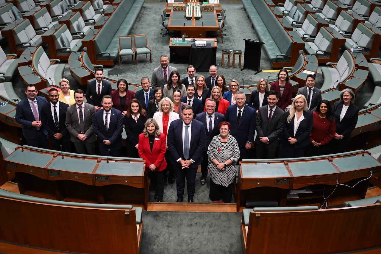 Men and women standing in the house of representatives, with their hands in front of them.